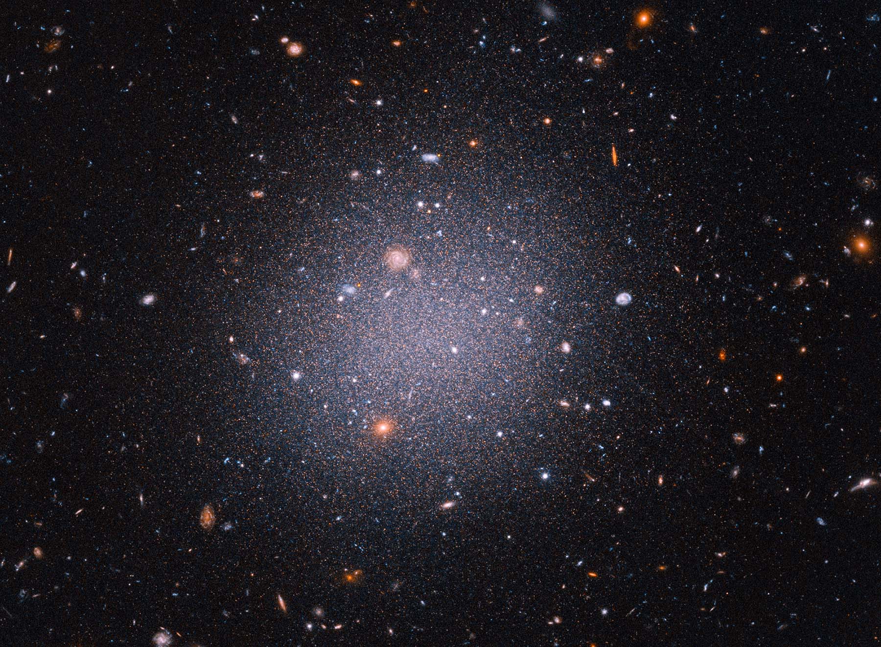 This Hubble Space Telescope snapshot reveals an unusual galaxy that researchers call a “see-through galaxy.” The giant cosmic cotton ball is so diffuse and its ancient stars are so spread out that distant galaxies in the background can be seen through it.