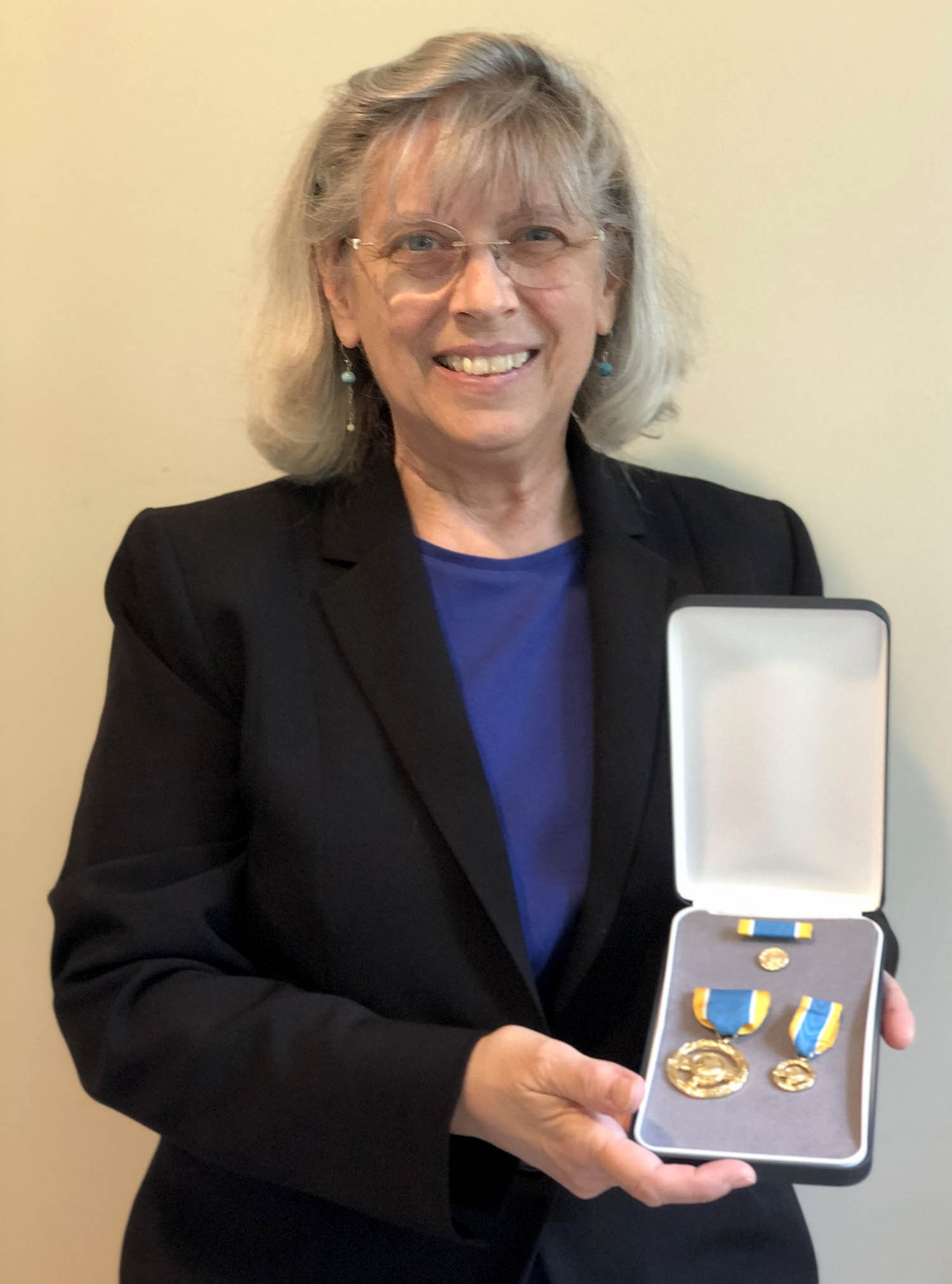 Dr. Heidi Hammel smiling and holding her medals from NASA in an open box.