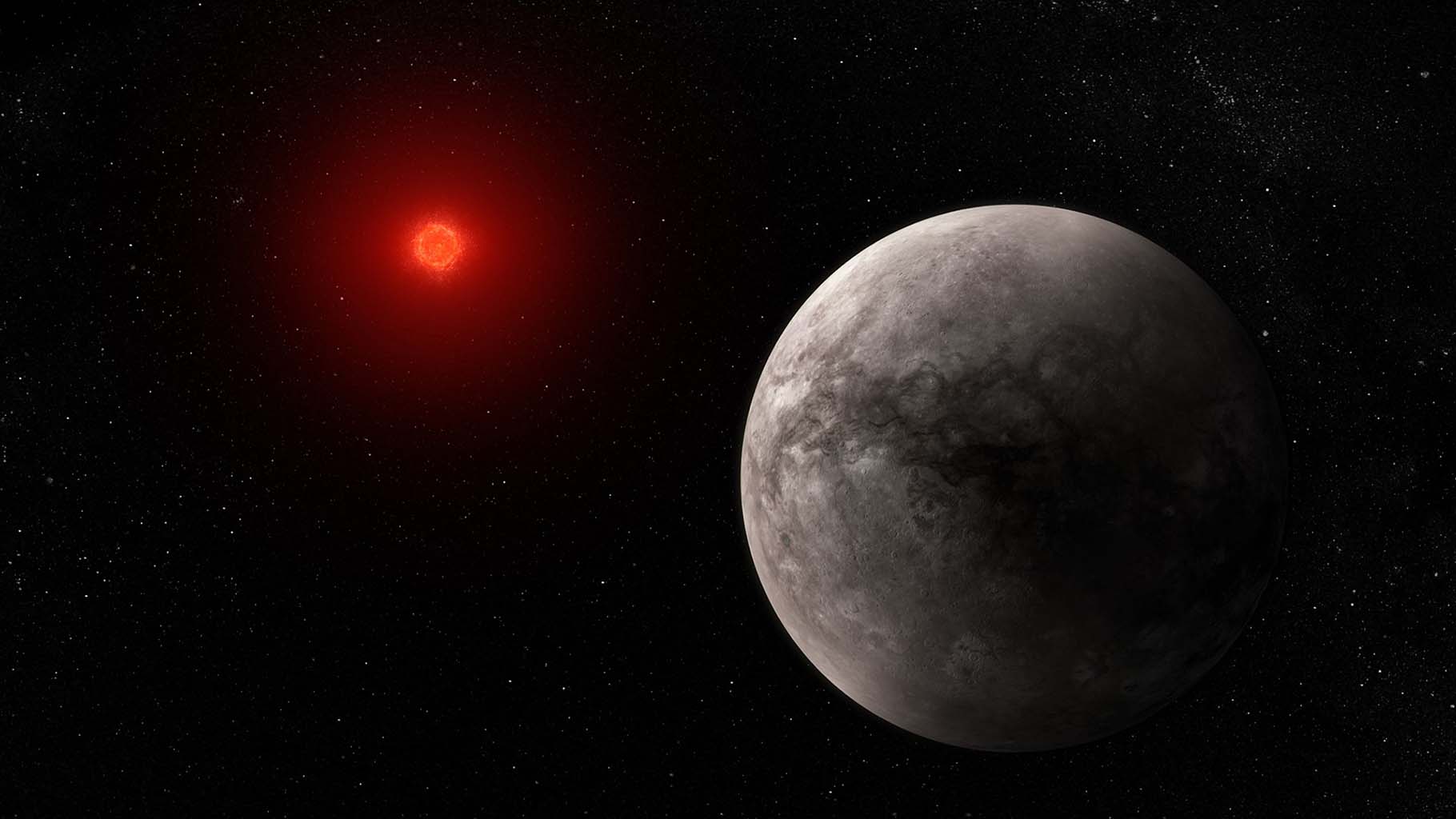 Illustration of a rocky planet and its red dwarf star on an empty black background. The planet is large, in the foreground on the lower right and the star is smaller, in the background at the upper left. The planet is various shades of gray, with some small craters. There is no apparent atmosphere. The left quarter of the planet (the side facing the star) is lit, while the rest is in shadow. The star has a bright orange-red glow, and appears to have a very active surface with multiple flares.