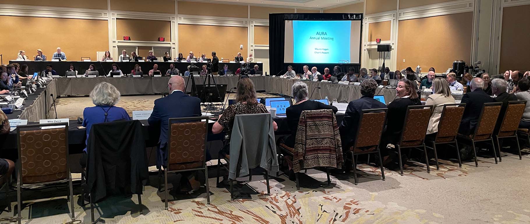 Participants sitting at  a square of tables about to being the meeting.