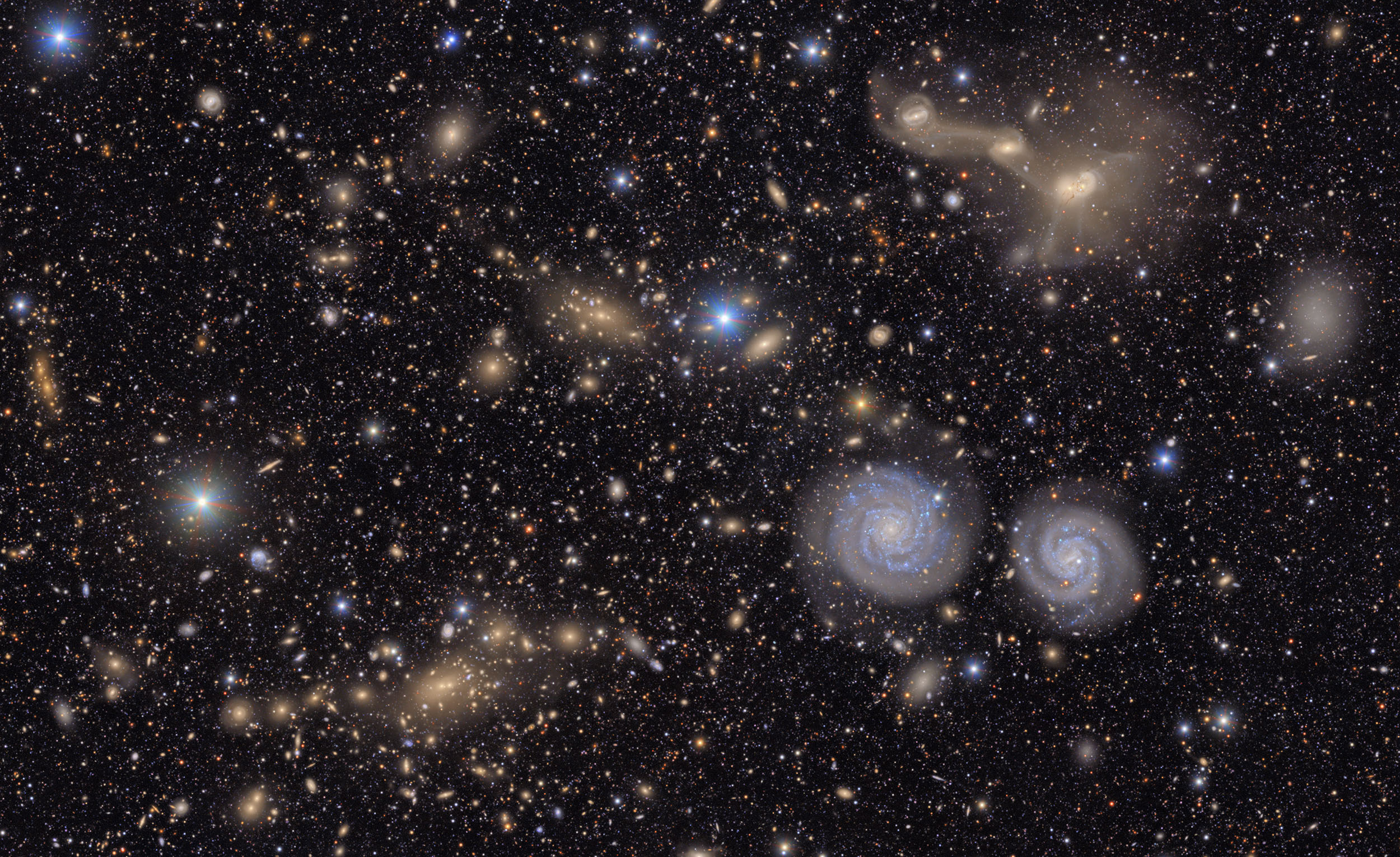 Many stars and galaxies including two spiral galaxies and three merging galaxies.