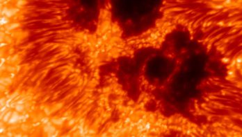 Undulating waves of gold, orange and red fill this image. Dark black areas are surrounded by deep red and orange indicating sunspots.