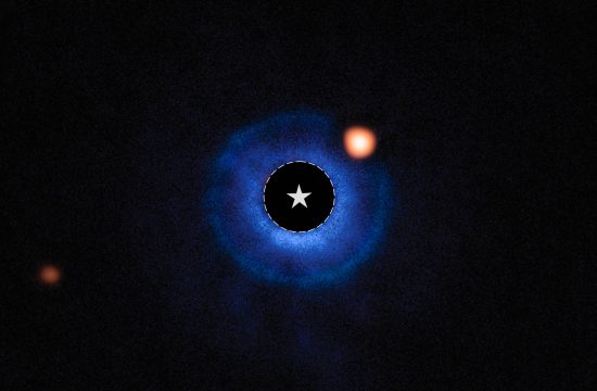 An image of a nearby star and its vicinity. The star itself has been blocked out and its bright light has been removed, appearing black. A dashed circle with a star symbol at the center of the image marks the star’s location. A fuzzy blue disk surrounds the star. An orange spot, near the star and inside this disk around 2 o’clock, is identified as a planet orbiting the star. A fainter orange spot at the lower left edge marks a distant star.