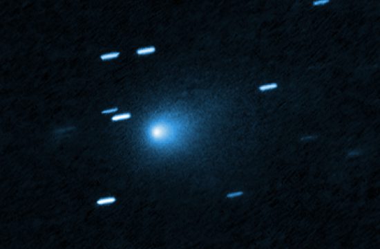 At the center of the image is a comet that appears as a teardrop-shaped bluish cocoon of dust coming off the comet’s solid, icy nucleus and seen against a black background. The comet appears to be heading to the bottom left corner of the image. About a dozen short, light blue diagonal streaks are seen scattered across the image, which are from background stars that appeared to move during the exposure because the telescope was tracking the moving comet.