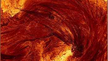 A close up image of the Sun with an orange wave-like structure in th middle and bright yellow sections above and below ir. It is covered in dark lines indicating the direction of the wave.
