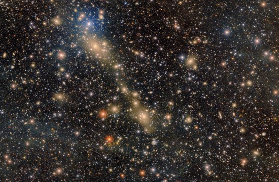 A glittering diagonal group of glowing yellow galaxies shine out of the image filled with glowing points of light.