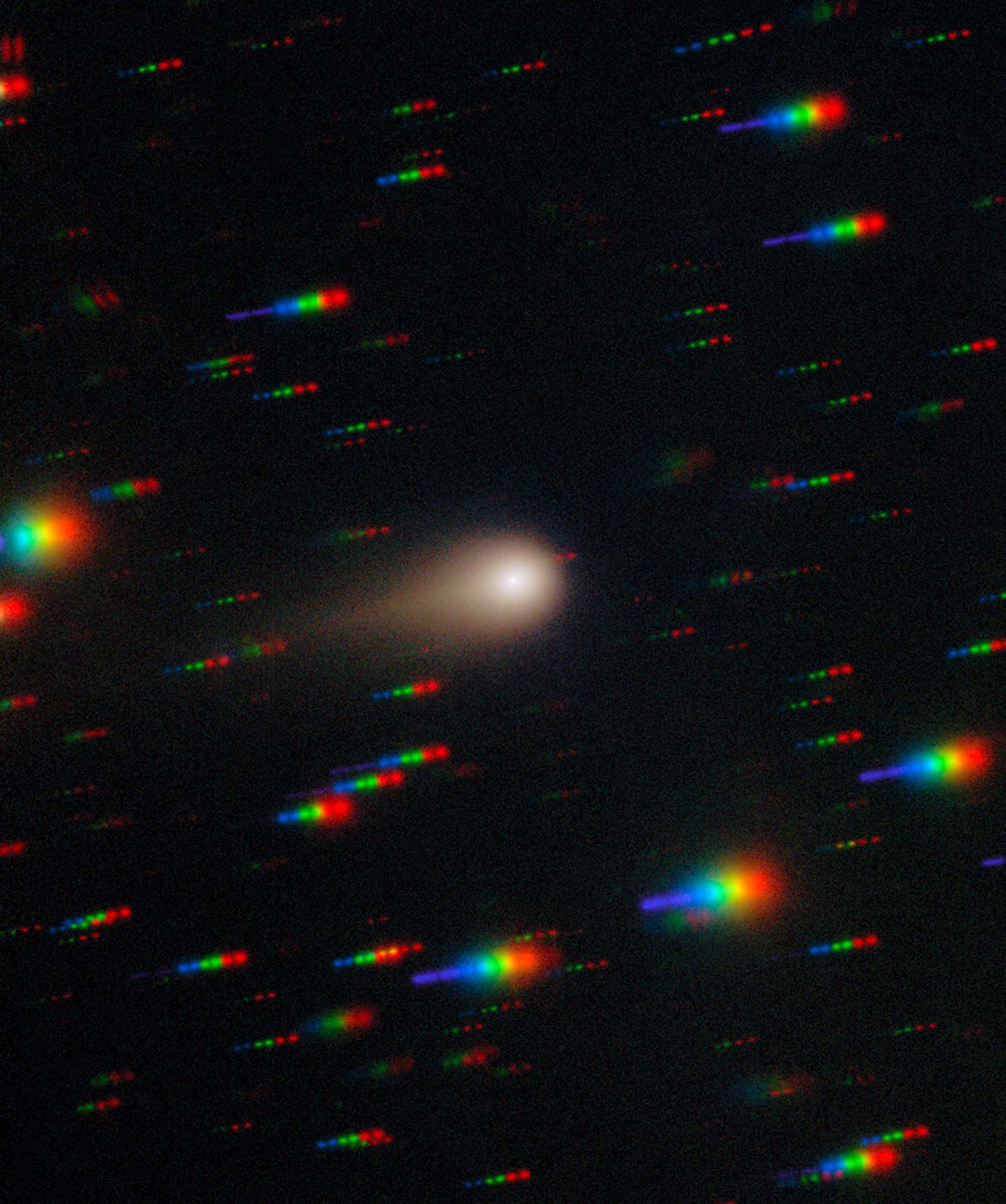 A glowing ball with a gold halo and tail streaks to the right in the center of this image. The black background is cover with rainbow colored streaks throughout the image.