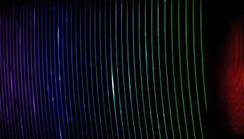 Slightly curved thin luminous lines from purple to turquoise to green to red and then yellow, run vertically over on a black background.