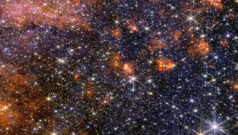 A wide view of a region of space filled with stars and clumps of orange clouds.
