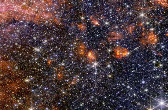 A wide view of a region of space filled with stars and clumps of orange clouds.