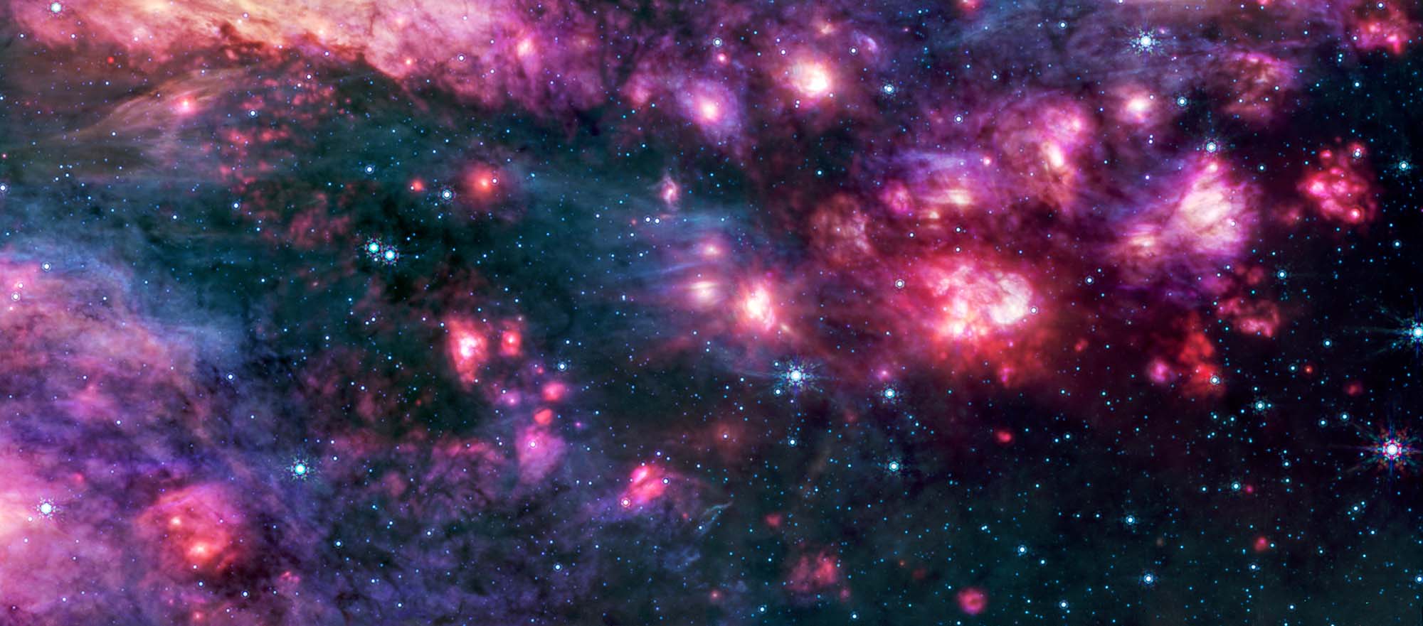 Cosmic clouds of pink and purple, some with bright centers, are surrounded by dark areas that appear like black space dotted with bright blue stars. A group of small clouds to the right is more red than any other area of the image.