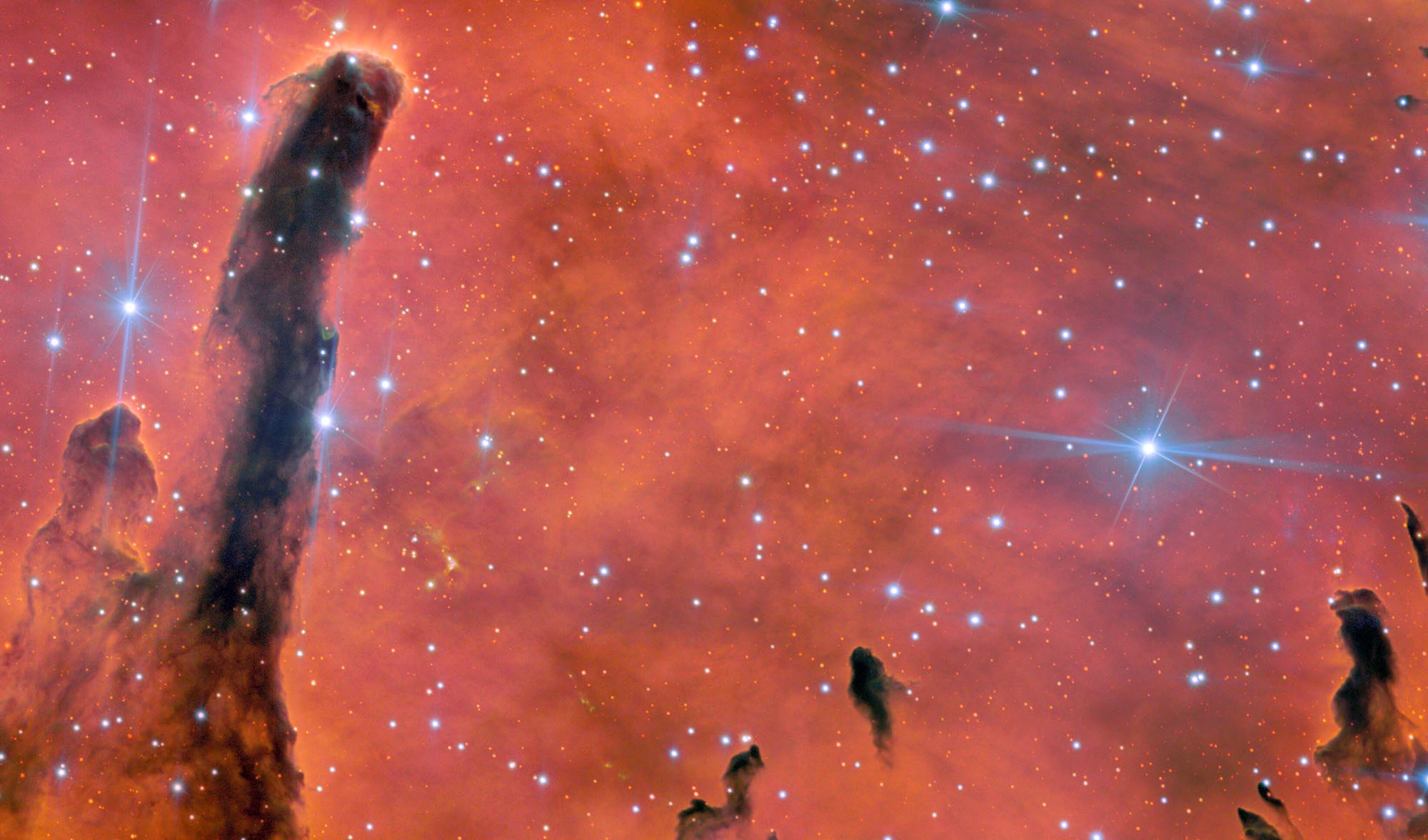 Ua ʻŌhiʻa Lani: An Image to Celebrate Gemini North’s 25th Anniversary features a red-orange background dotted by stars. Tall dark pillars of gas and dust rise in the foreground.