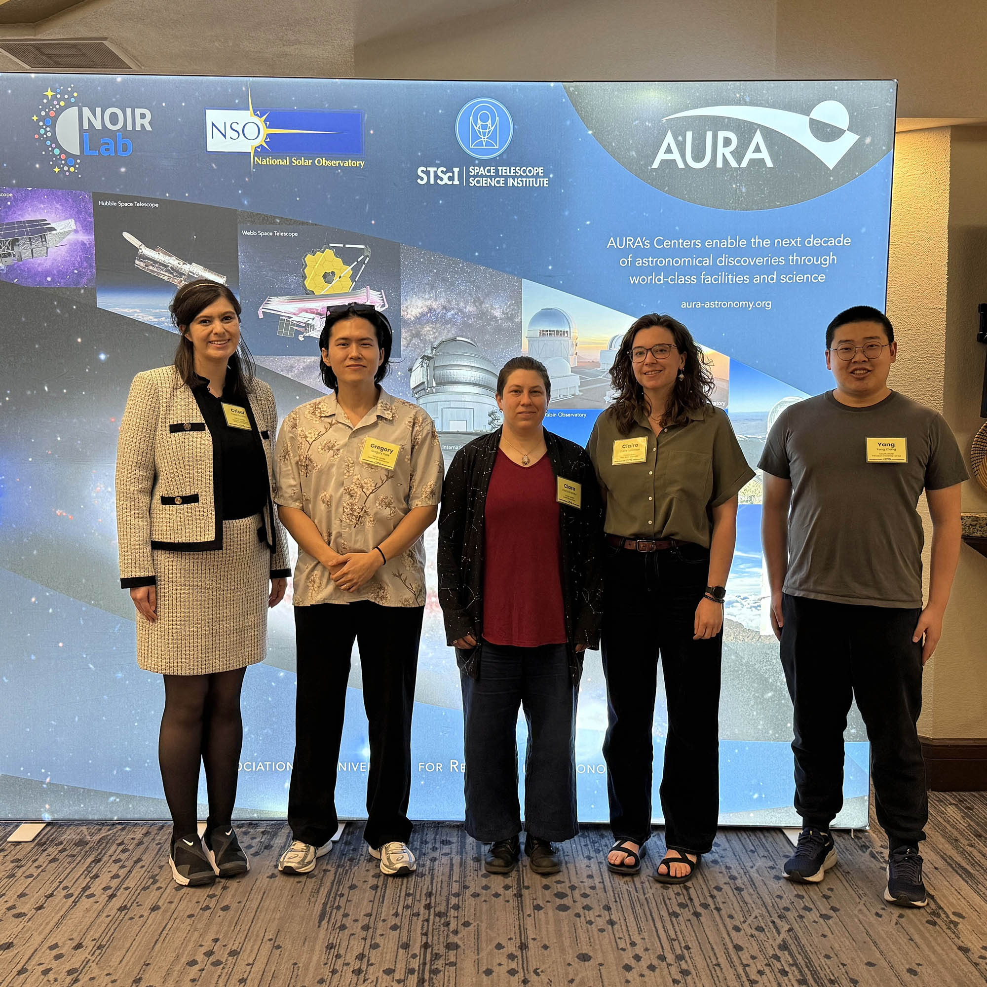 A group of early career astronomers stand in front of a colorful display showing astronomical images and telescopes.