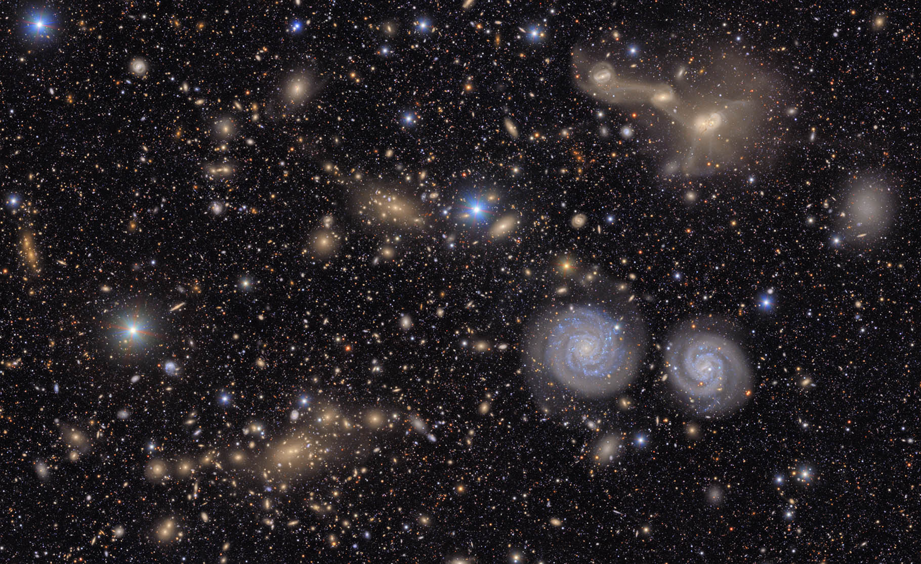 an amazing plethora of stars and galaxies on a black background fill this image. 2 swirling galaxies on the right of the image.