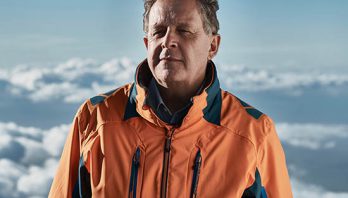 Man in orange jacket with a blue and cloudy sky behind him