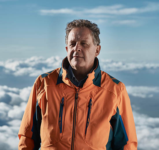 Man in orange jacket with a blue and cloudy sky behind him