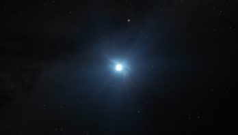 Illustration showing a small circular white object on the black background of space speckled with dim stars. The object is glowing, and rays of soft light emanate in all directions. The words “Artist’s Concept” are at the lower right.