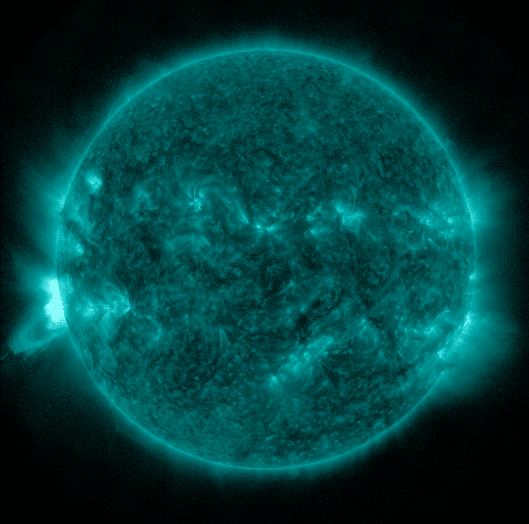 A full-disk extreme ultraviolet visualization of the Sun rendered in a brilliant, textured cyan-teal hue against a black background. The solar surface is covered in intricate, mottle patterns with darker filimentary structures and multiple smaller bright active regions. On the lower-left edge, a blindingly bright white-cyan eruption—a long-duration M-class solar flare—is actively exploding from the limb, with brilliant hot plasma and detailed magnetic loops extending into the void of space, originating from a region just beyond the Sun's edge.